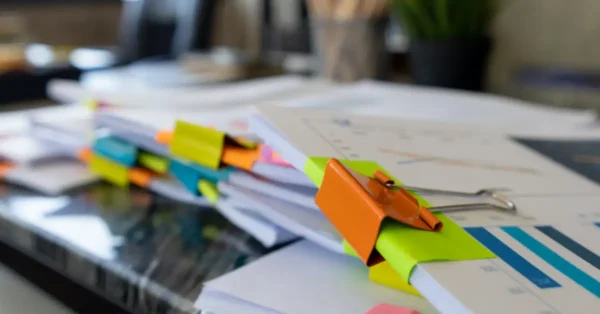 Piles of documentation held together by colorful binder clips. This image represents the increased documentation that management will need to provide for 2023 audits.