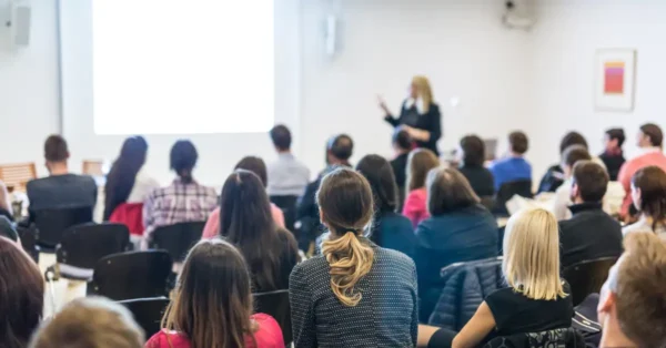 A large group listening to a female speaker - to represent employees learning about their employer sponsored benefits