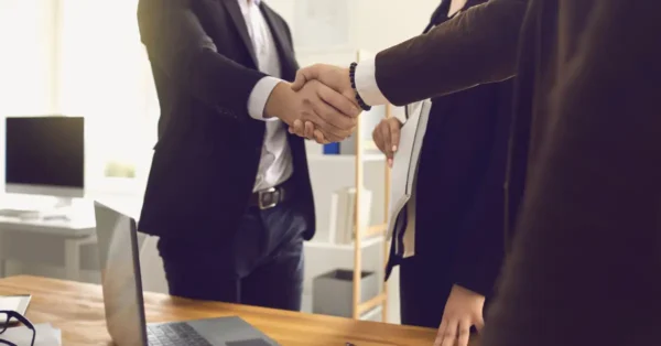 Two men in black suits, shaking hands to represent a negotiation or agreement