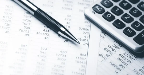 Picture of financial statements with a black pen on top and a calculator in the top right corner.