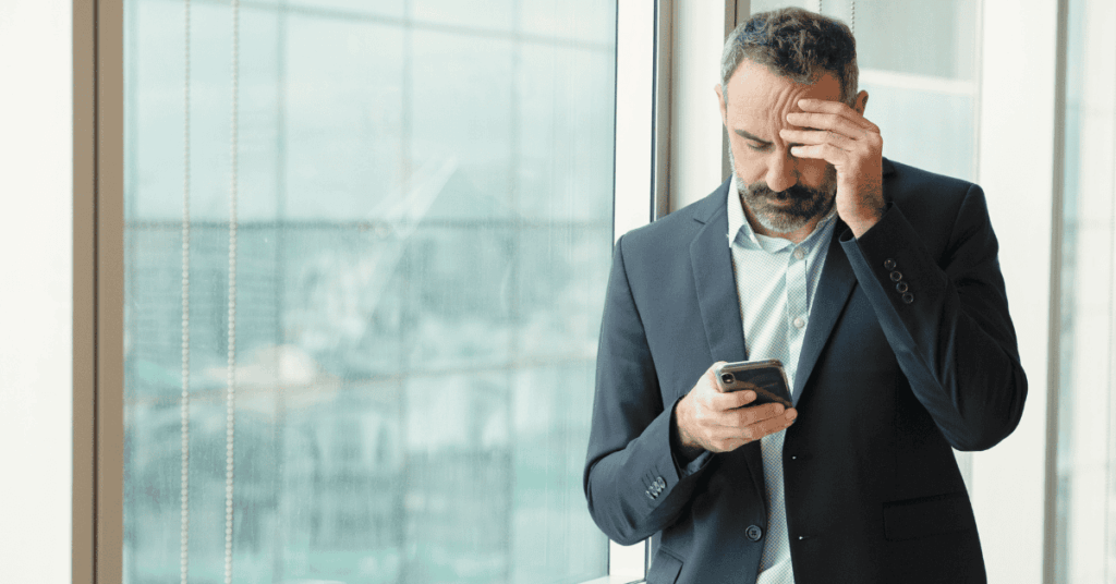 A man, looks at his phone, head down, and obviously worried as he is late to file his taxes.
